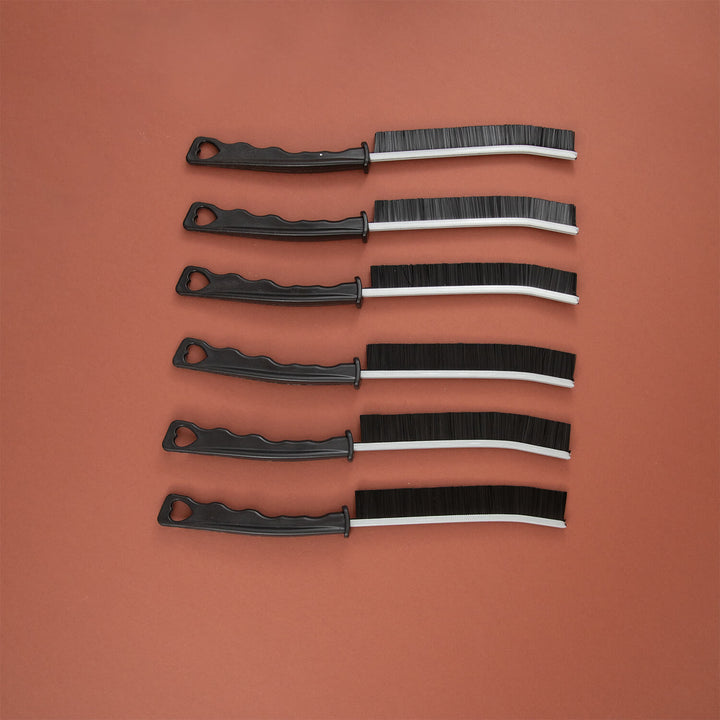 Set of five black and white crevice cleaning tools, microfibre, cleaning supplies, cleaning brushes arranged on a brown background