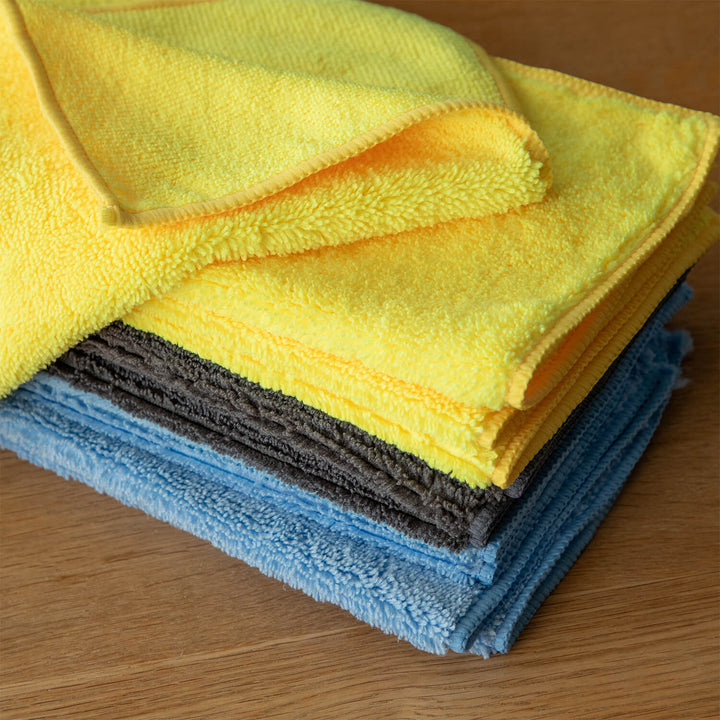 Stack of yellow, blue, and gray microfiber cleaning cloths, microfibre, cleaning cloths, cleaning supplies on a wooden surface