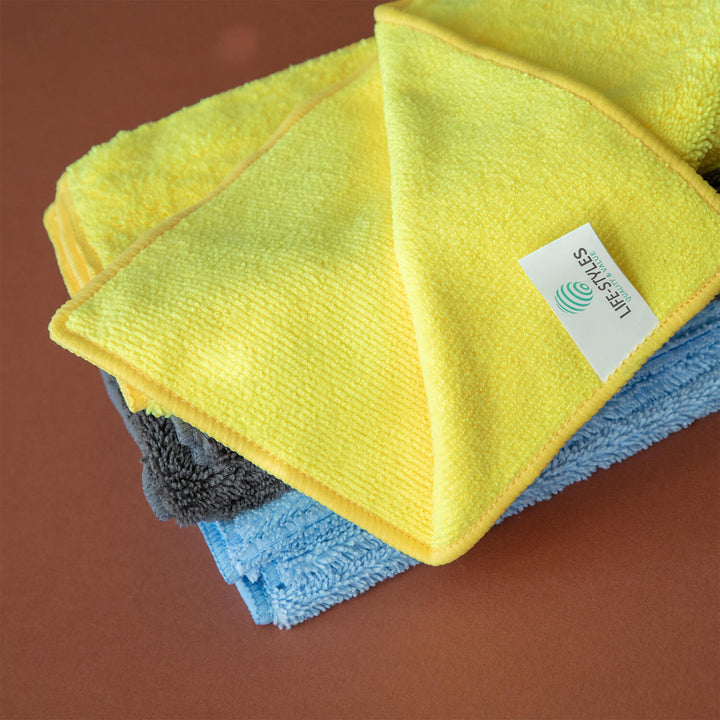 Three microfiber cloths, microfibre cleaning cloths, cleaning supplies, cleaning tools in yellow, blue, and gray with a brand label on a brown background.