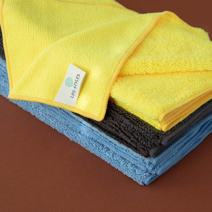 Stack of yellow, blue, and gray microfiber cloths, cleaning supplies, cleaning cloths, microfibre with a visible brand label on a brown background.