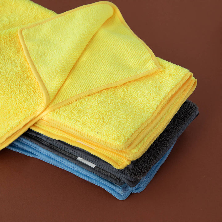 Stack of yellow, blue, and gray microfiber cloths, microfibre cleaning cloths, cleaning supplies on a brown background