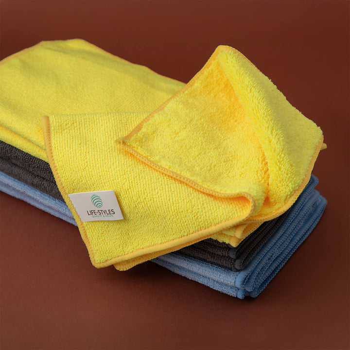 Stack of yellow, gray, and blue microfiber cloths, microfibre cloths, cleaning supplies, cleaning cloths with a visible brand logo on a brown background