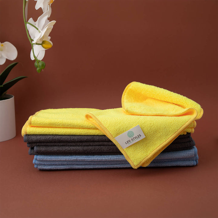 Stack of yellow, gray, and blue microfiber cloths, microfibre cloths, cleaning supplies, cleaning cloths with a visible brand label on a brown background.