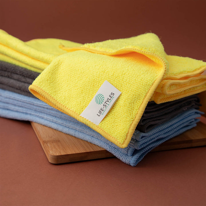 Stack of yellow, gray, and blue microfiber cloths, microfibre cloths, cleaning supplies on a wooden block with 'LIFE-STYLES' branding.