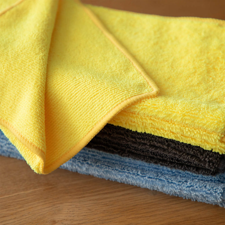 Stack of yellow, blue, and black microfiber cloths, microfibre cloths, cleaning cloths, cleaning supplies on a wooden surface