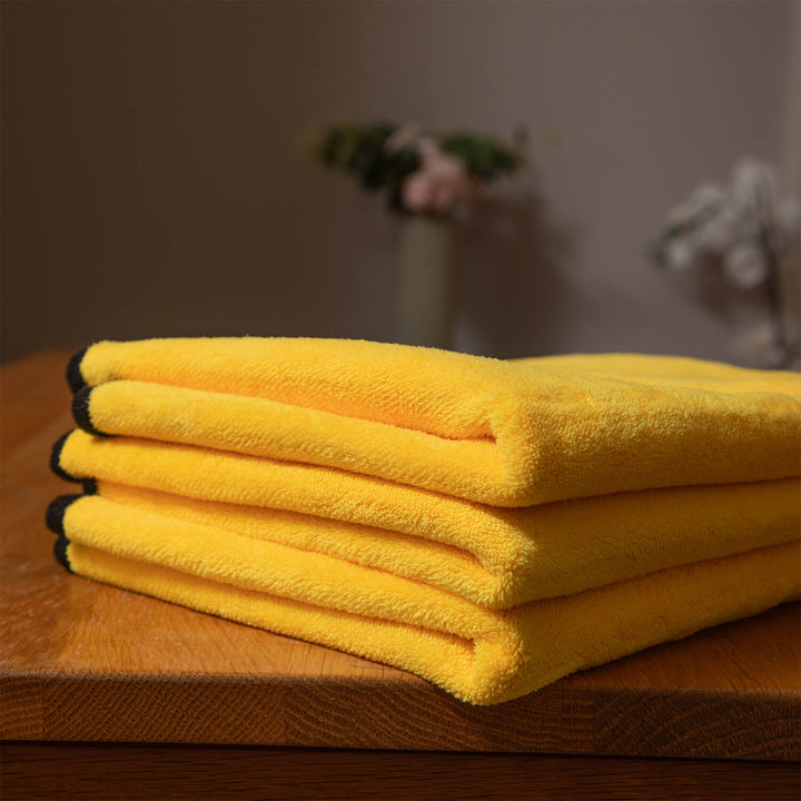 Stack of 3 yellow microfibre cloths, cleaning supplies, cleaning cloths on an wooden table