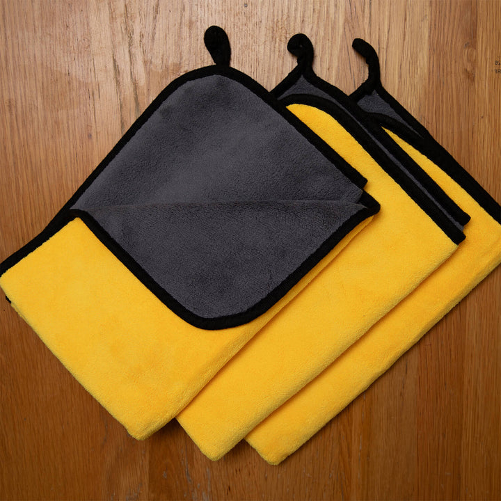 Three microfibre cleaning cloths, cleaning supplies, cleaning cloths, microfibre two yellow and one black, on a wooden surface.