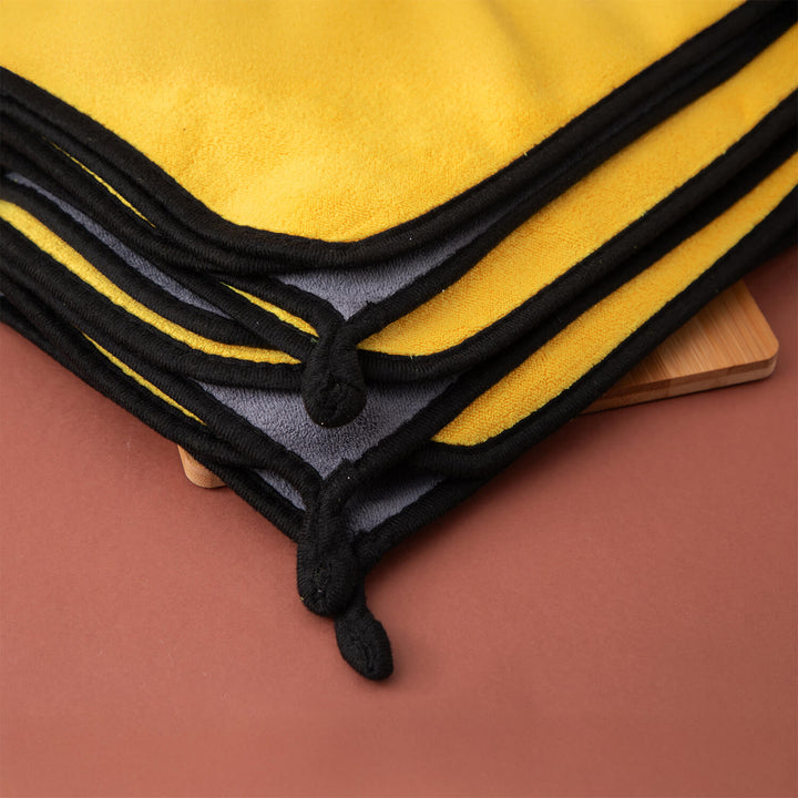 Yellow microfibre cleaning cloths, cleaning supplies, cleaning cloths with black trim folded on a wooden surface