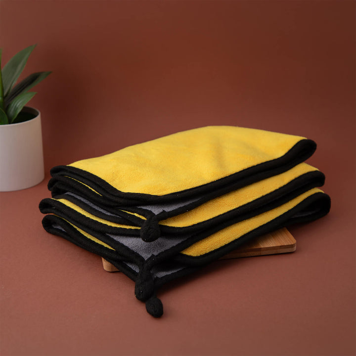 Stack of yellow and black microfibre cleaning cloths, cleaning supplies, cleaning cloths on a brown surface with a plant in the background